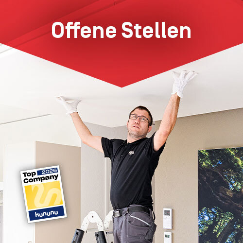 Mitarbeiter Realisation der Deckenflieger-Crew von Röösli Funktionsdecken bei der Montage einer Funktionsdecke. Die rote angeschnittene Raute als Gestaltungselement von Röösli Funktionsdecken enthält den Text «Offene Stellen». Zusätzlich mit dem Top Company Siegel von Kununu.