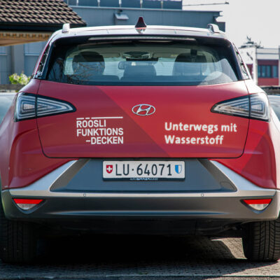 Das Heck eines Röösli Autos ersichtlich mit der Aufschrift "Unterwegs mit Wasserstoff" und dem Röösli Funktionsdecken-Logo. Röösli Funktionsdecken.